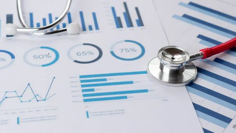 A stethoscope rests on sheets of paper displaying various blue bar graphs, pie charts, and statistical data, suggesting a focus on healthcare analytics or medical statistics.