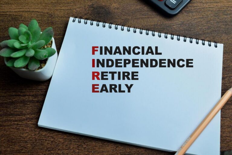 A notepad on a wooden desk displays the acronym FIRE, standing for Financial Independence Retire Early, with each word listed underlined in black and the red letters forming FIRE. A succulent and pencil are nearby.